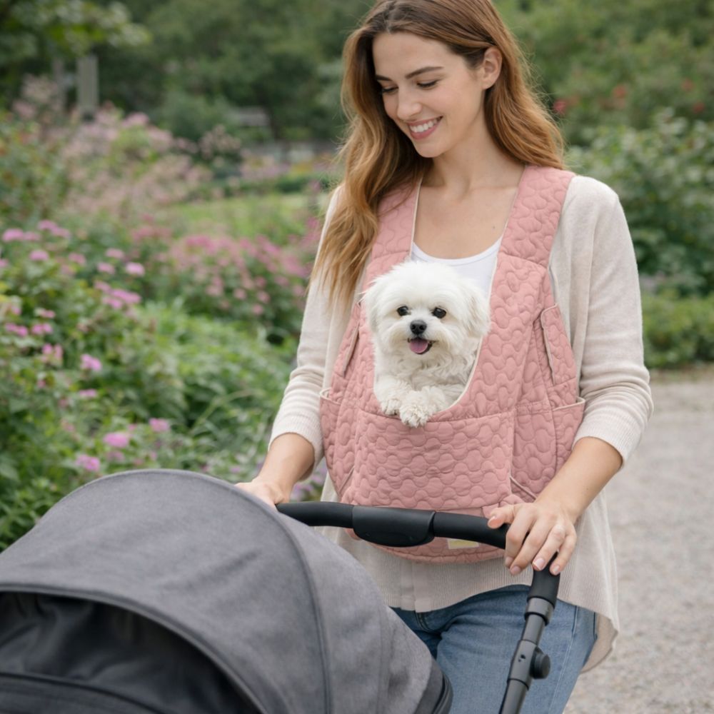 Maman portant un petit bichon dans un sac ventral pour chien, se promène dans un jardin avec son bébé dans la poussette