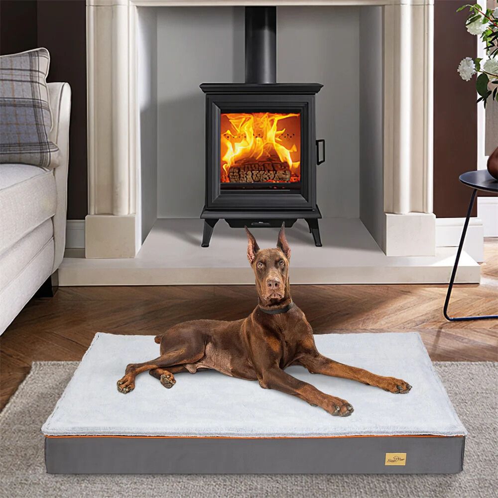 Doberman allongé sur un tapis chien XXL à mousse épaisse, placé devant une cheminée
